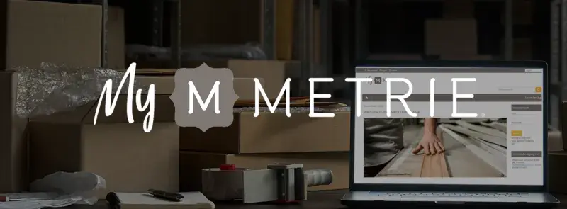 A warehouse full of cardboard boxes with a laptop on a desk. The laptop shows the landing page to "My Metrie.com. The logo for "My Metrie" is overlaid over top.